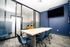 Modern conference room with sleek glass walls, a long table, and blue chairs, perfect for meetings and presentations.