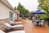 Expansive wooden deck with stylish lounge chairs and round outdoor tables under blue umbrellas, surrounded by lush greenery, perfect for relaxation and entertaining.