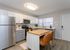 Modern kitchen featuring stainless steel appliances, elegant cabinetry, and a wooden island with leather chairs, bathed in natural light.