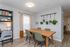 Contemporary dining area with stylish wooden table, green upholstered chairs, hanging plants, and ambient bookshelf lighting for a cozy atmosphere.