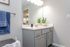 Bright and modern bathroom with sleek gray cabinetry, elegant countertop, and cozy lighting. Stylish accents include blue towels and lush greenery.