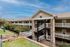 Charming apartment complex with elegant stone facade, inviting white railings, and lush greenery under a bright blue sky.