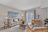 Bright and inviting living room with elegant beige sofas, artistic wall decor, and natural light streaming through patio doors, perfect for relaxation and entertainment.