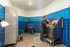 Modern pet grooming facility with bright blue tiled walls, featuring a smiling golden retriever being bathed by a friendly staff member in a stainless steel tub, creating a welcoming and well-equipped atmosphere.