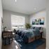Cozy bedroom featuring modern decor, a stylish blue bedspread, natural light from a large window, and a charming study nook.