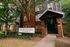 Inviting entrance of Lyons Corner Apartments with charming brick and wood facade, surrounded by lush greenery.