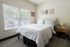 Inviting bedroom with a plush bed, two large windows letting in natural light, and stylish wall decor, perfect for relaxation.