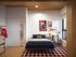 Modern bedroom with chic decor, featuring a cozy bed, stylish artwork, and a bright workspace overlooking the city.