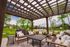 Charming outdoor patio with rustic pergola, cozy seating, and picturesque view of lush greenery and serene neighborhood.