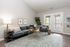Elegant living room with a plush gray sectional, stylish round coffee tables, and abundant natural light from large patio doors. Accented by lush greenery and contemporary artwork.