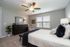 Bright and inviting bedroom featuring a luxurious bed, elegant dresser, and cozy reading nook, complemented by a ceiling fan and natural light.