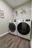 Modern laundry room with sleek front-loading washer and dryer on elegant wooden floors, featuring tasteful wall art and practical shelving.