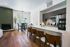 Modern living space featuring a sleek kitchen with marble countertops, cozy dining area, and elegant wooden floors. Abundant natural light and a chic workspace create a welcoming atmosphere.