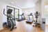 Modern fitness center with state-of-the-art treadmill, exercise bike, and elliptical, accented by sleek wooden flooring and abundant natural light.