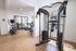 Modern apartment gym with exercise equipment, including a treadmill, elliptical, and weight machine, in a bright and airy space with hardwood flooring.