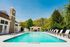 Inviting outdoor pool area with modern loungers, surrounded by lush greenery and a charming stone clubhouse.