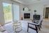 Bright living room with modern decor, featuring a cozy fireplace, elegant glass coffee tables, and a balcony with a scenic view.