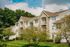 Charming apartment building with stylish stone facade surrounded by lush greenery and blue skies, offering serene living.