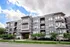 Modern apartment building with stylish brick facade and large windows, surrounded by lush greenery on a sunny day.