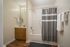 Elegant bathroom boasting a modern shower with a stylish grey curtain, sleek vanity with lighting, and warm wooden flooring.