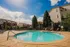 Charming apartment complex with a sparkling pool, surrounded by lush greenery and modern buildings under a clear blue sky.