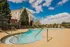 Charming apartment complex with a serene swimming pool, surrounded by lush greenery and bright blue skies.