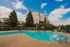 Charming residential building with a sparkling outdoor pool, surrounded by lush greenery and vibrant blue skies, ideal for relaxation.
