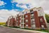 Elegant multi-story apartment building with charming brick facade, spacious balconies, and lush greenery under a vibrant blue sky.