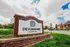Inviting entrance to Devonshire Apartments, featuring a modern brick sign surrounded by lush greenery and residential buildings under a bright sky.