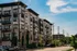Charming mid-rise apartment building with modern balconies and lush greenery, set against a bright blue sky.