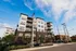 Contemporary apartment building with modern architecture, showcasing large windows and elegant balconies, set against a bright blue sky.