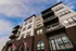 Modern apartment facade featuring multiple balconies and stylish brickwork against a vibrant blue sky.
