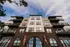 Impressive modern apartment building with elegant brick facade, stylish balconies, and vibrant flags set against a clear blue sky.