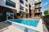 Inviting outdoor pool area surrounded by modern apartment building with stylish loungers and vibrant red umbrellas, perfect for relaxation and enjoyment.