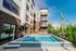 Modern apartment complex with a refreshing outdoor pool and sun loungers under clear blue skies, offering a perfect blend of leisure and urban living.