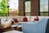 Inviting outdoor patio featuring cozy beige sectional sofa with vibrant cushions, surrounded by lush greenery and brick walls.
