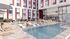Luxurious apartment complex with a stylish outdoor pool, featuring elegant lounge chairs, vibrant umbrellas, and a lively barbecue area.