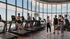 Modern fitness center with panoramic city views, featuring people engaging on treadmills and socializing, creating an energetic and vibrant atmosphere.