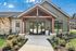 Charming apartment entrance with modern design, featuring lush landscaping and inviting glass doors under a stylish gabled roof.