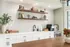 Chic kitchen space with elegant white cabinetry, modern shelves, and stylish tile backsplash featuring decorative books and plants.