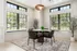 Bright dining nook with a modern round table and four plush chairs, accented by large windows and lush greenery for a serene atmosphere.