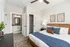 Inviting bedroom with modern decor, featuring a cozy bed with blue accents, stylish artwork, and en-suite access to a bathroom. Bright and airy ambiance with elegant furnishings.