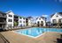 Contemporary apartment complex with inviting pool and sun loungers, set against a clear blue sky.