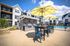 Charming outdoor space with sunny yellow umbrellas, modern barbecue grills, and inviting seating area by a sparkling pool.