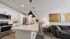 Modern kitchen and living area featuring sleek pendant lights, stylish artwork, and a comfortable gray sofa in an open-concept space.