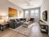 Bright and modern living room featuring a comfortable grey sofa, stylish artwork, and large sunlit windows.