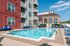Inviting apartment complex with a sparkling outdoor pool, vibrant lounge chairs, and modern architecture under a clear blue sky.