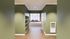 Inviting hallway leading to a sunlit gym with large windows and modern workout equipment, accented by elegant green walls.