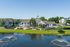 Scenic view of modern apartment complex with a vibrant community area, lush greenery, and serene pond with fountains.