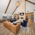 Spacious and elegant living area featuring a high vaulted ceiling, modern chandelier, cozy fireplace, and stylish seating arrangements in warm tones and plush fabrics.